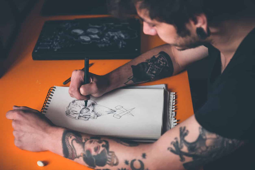 Young tattoo artist draw a new sketch on paper before tattooing Halloween Style Tattoo on skin